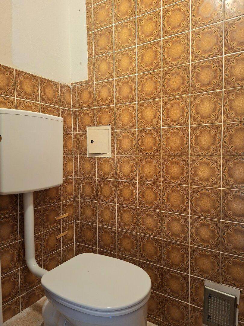 Toilette mit braunen, gemusterten Fliesen und einem Wand-WC.