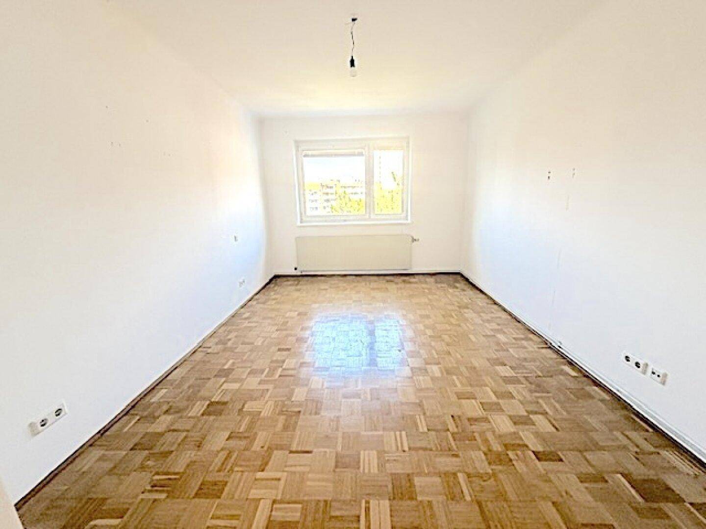Leeres Schlafzimmer mit Fischgrätparkett und weiß gestrichenen Wänden, bereit zur individuellen Gestaltung.