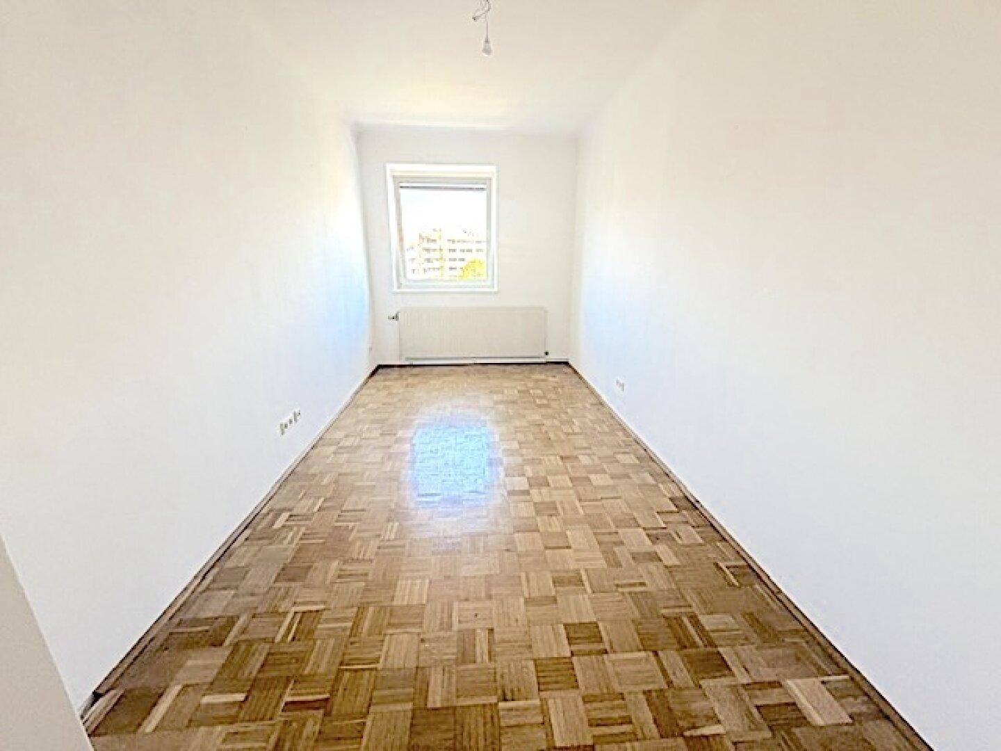 Leeres Schlafzimmer mit Fischgrätparkett und weiß gestrichenen Wänden, bereit zur individuellen Gestaltung.