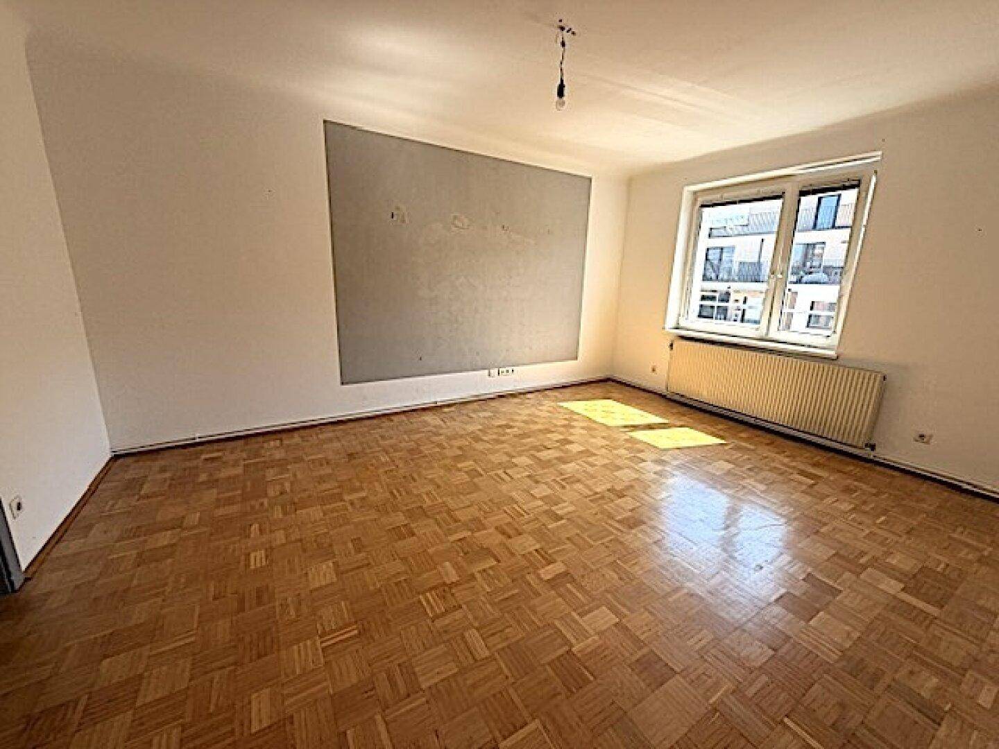 Großes, leeres Wohnzimmer mit Fischgrätparkett und einer Akzentwand, ideal für individuelle Einrichtung.