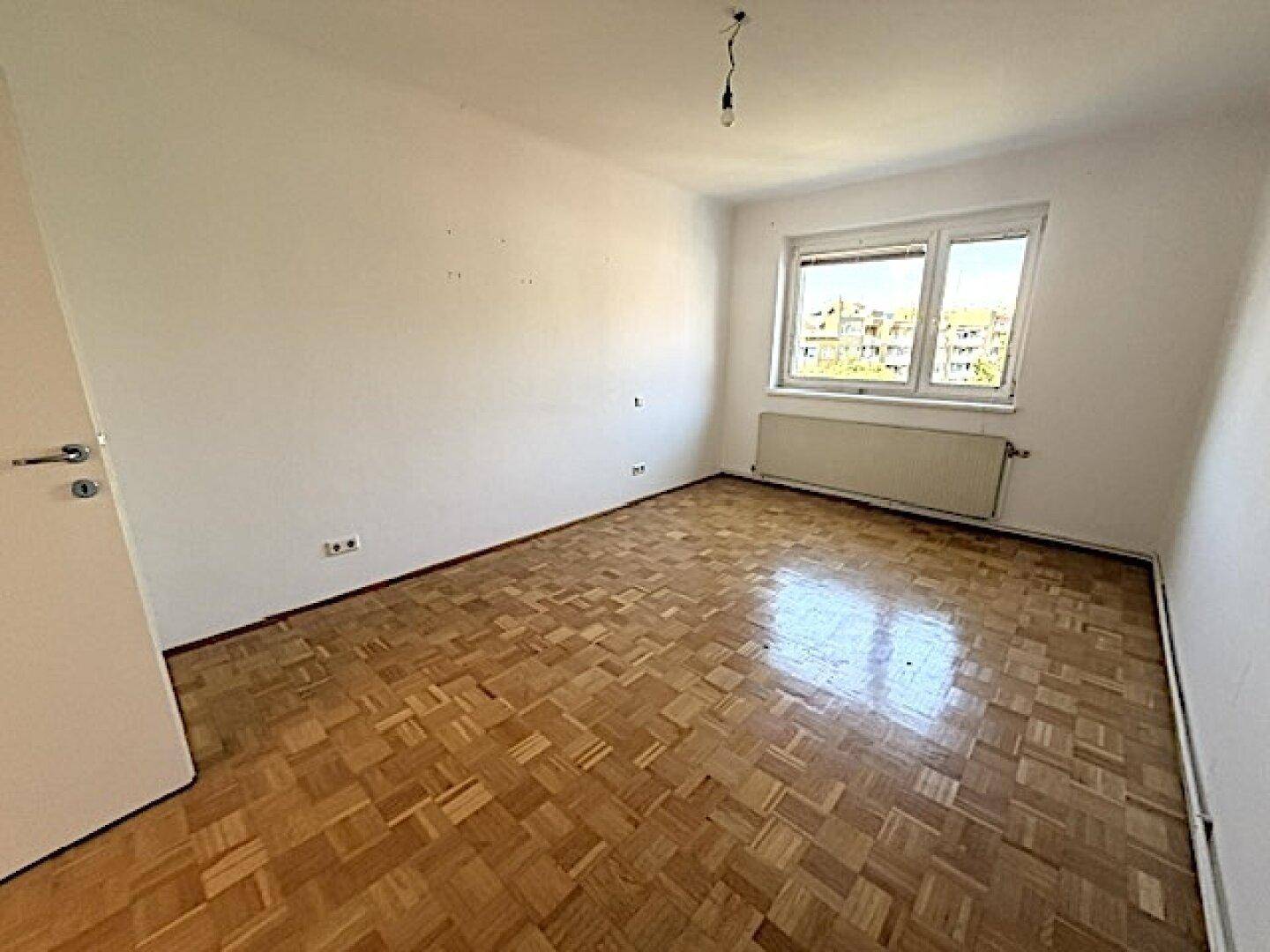 Helles, leeres Schlafzimmer mit Fischgrätparkett und Blick ins Grüne.