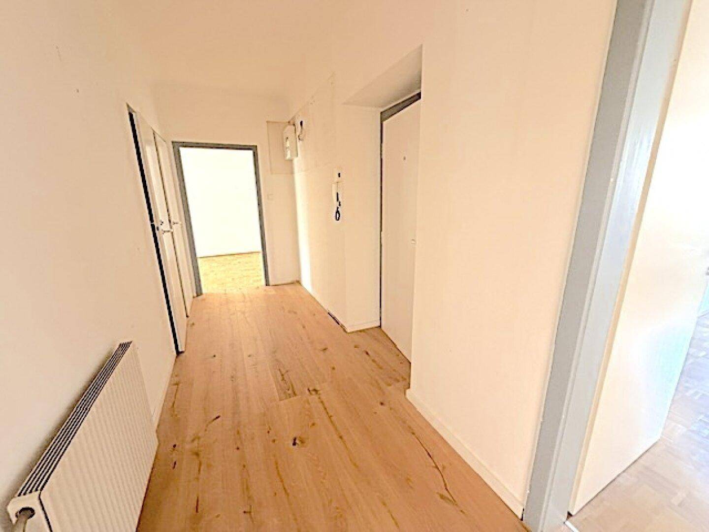 Heller Flur mit Holzdielenboden und Zugang zu verschiedenen Zimmern der Wohnung.