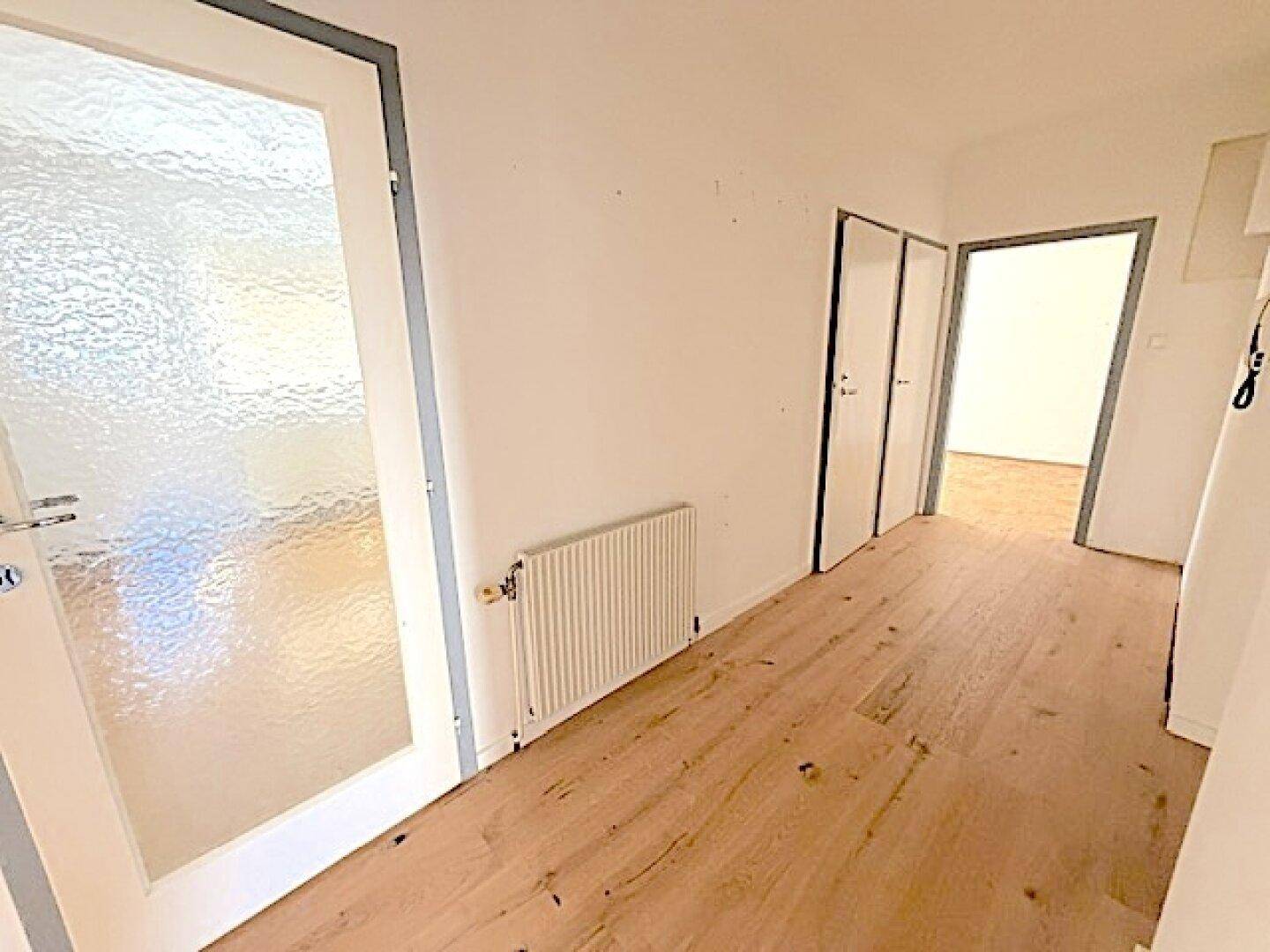 Eingangsbereich mit Holzdielenboden und einer Tür mit Milchglas, die Licht hereinlässt.
