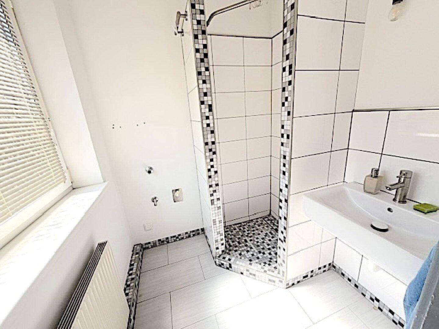 Modernes Badezimmer mit Duschkabine, Waschbecken und Fenster, hell gefliest.