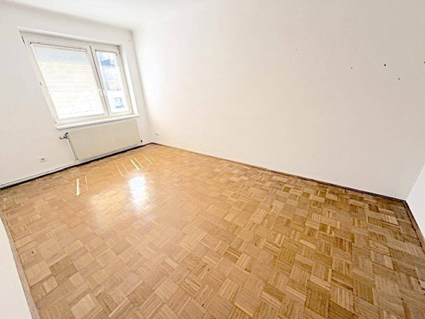 Helles, leeres Schlafzimmer mit Fischgrätparkett und weiß gestrichenen Wänden, bereit zur individuellen Gestaltung.