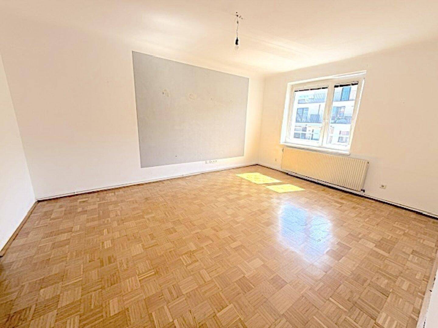 Großes, leeres Wohnzimmer mit Fischgrätparkett und einer Akzentwand, ideal für individuelle Einrichtung.