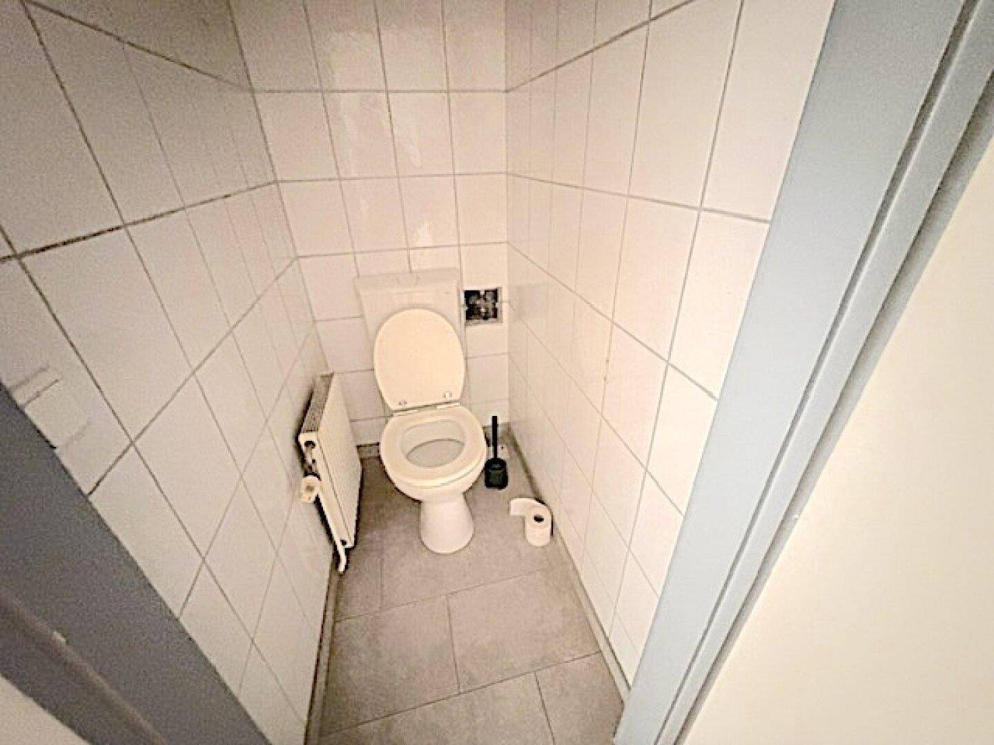 Separates WC mit Toilette und Heizkörper, komplett gefliest in Weiß.