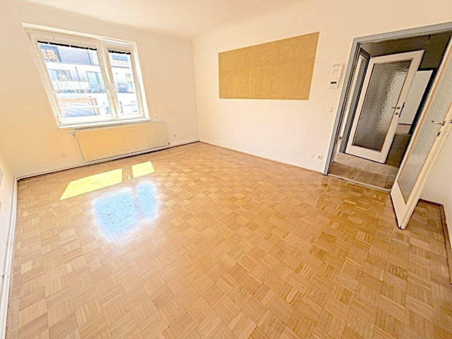 Helles, leeres Wohnzimmer mit Fischgrätparkett und Zugang zum Flur, bereit zur Gestaltung.