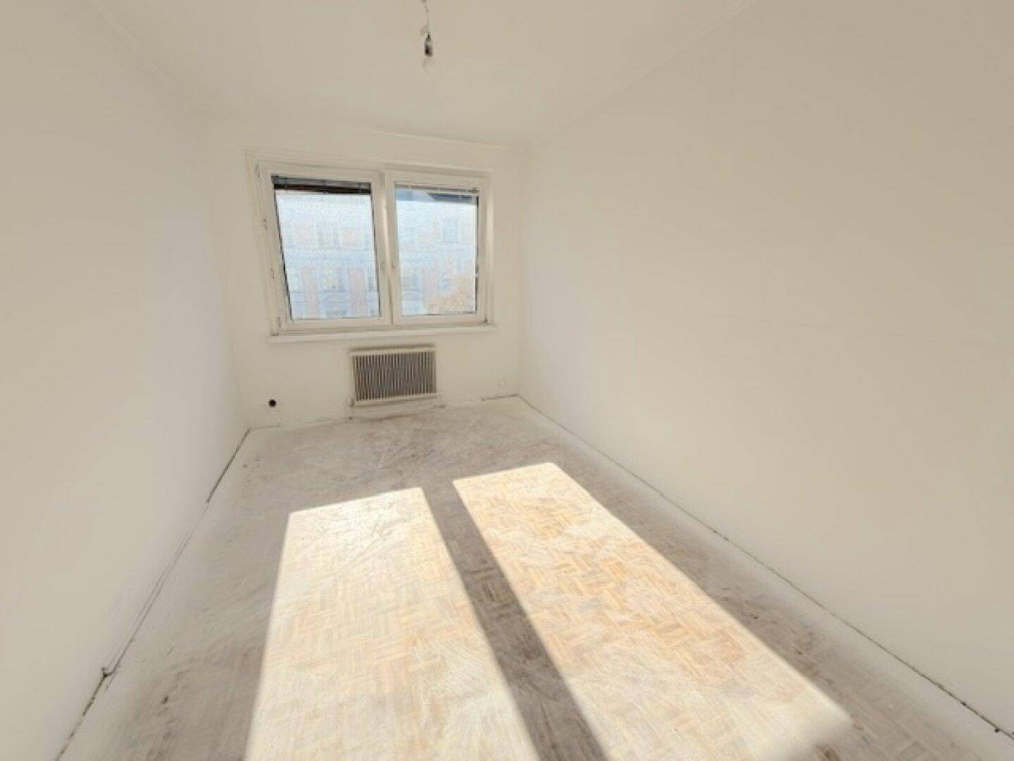 Sonniger Raum mit weiß gestrichenen Wänden und einem Fenster, das viel Tageslicht hereinlässt.