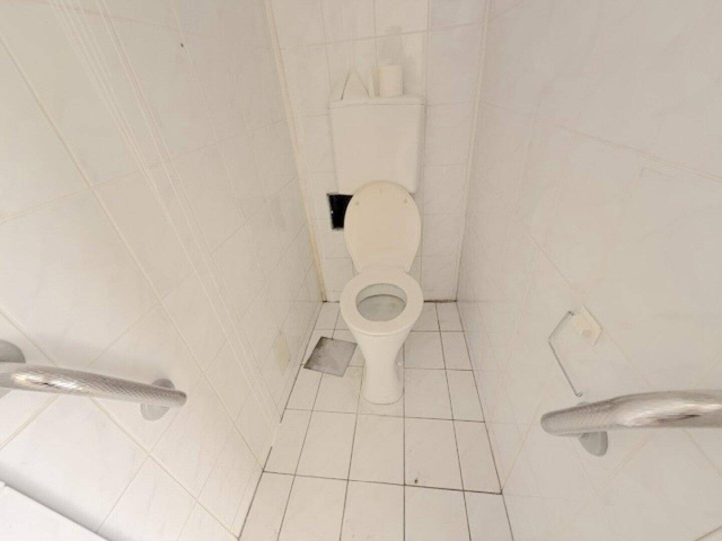 Kleines WC mit weißen Fliesen, Toilette und Haltegriffen für zusätzliche Sicherheit.