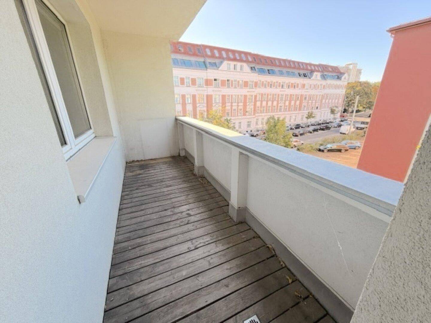 Balkon mit Holzboden und Blick auf die gegenüberliegende Wohnbebauung.