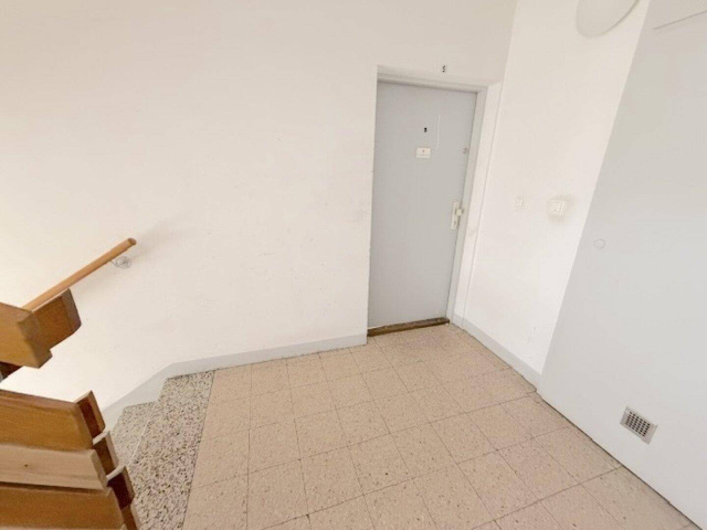 Treppenhausabsatz mit Fliesenboden, Holzgeländer und einer Eingangstür zur Wohnung.