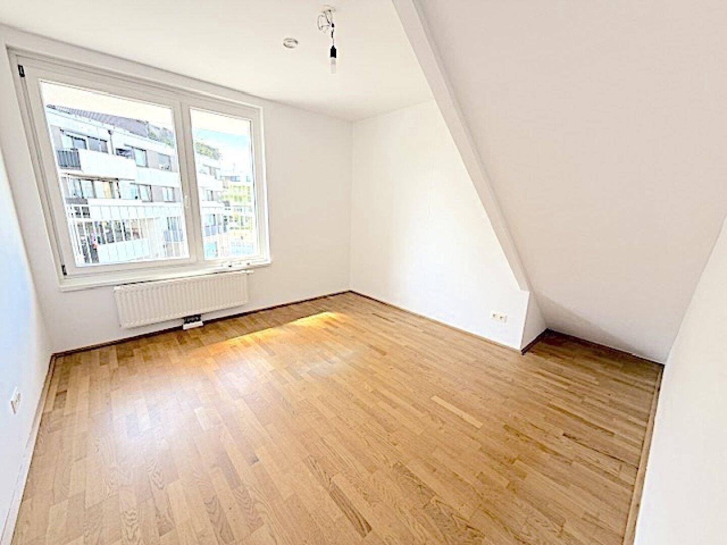 Leeres Zimmer mit Holzboden, großen Fenstern und Dachschräge, ideal als Schlafzimmer.