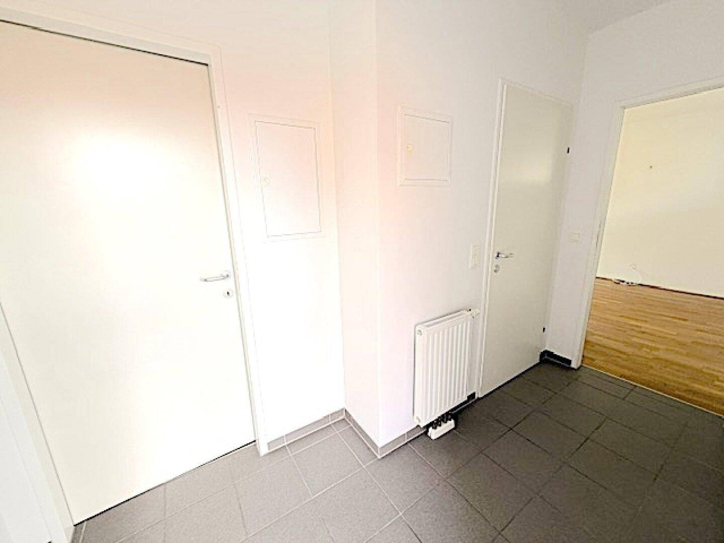Heller Flur mit grauen Fliesen und weißen Türen, der zu weiteren Räumen führt.