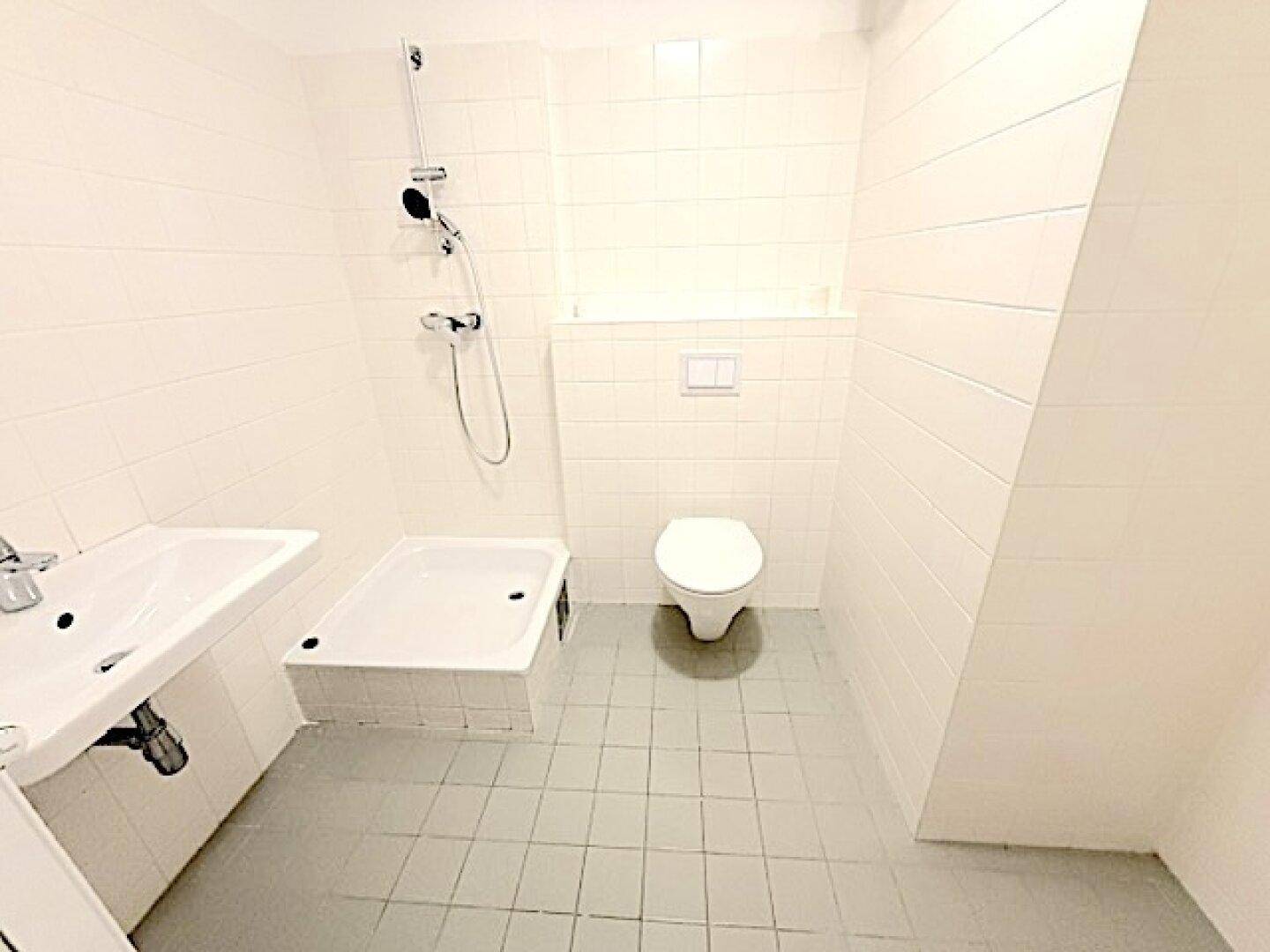 Funktionales Badezimmer mit Dusche, WC und Waschbecken, hell gefliest.