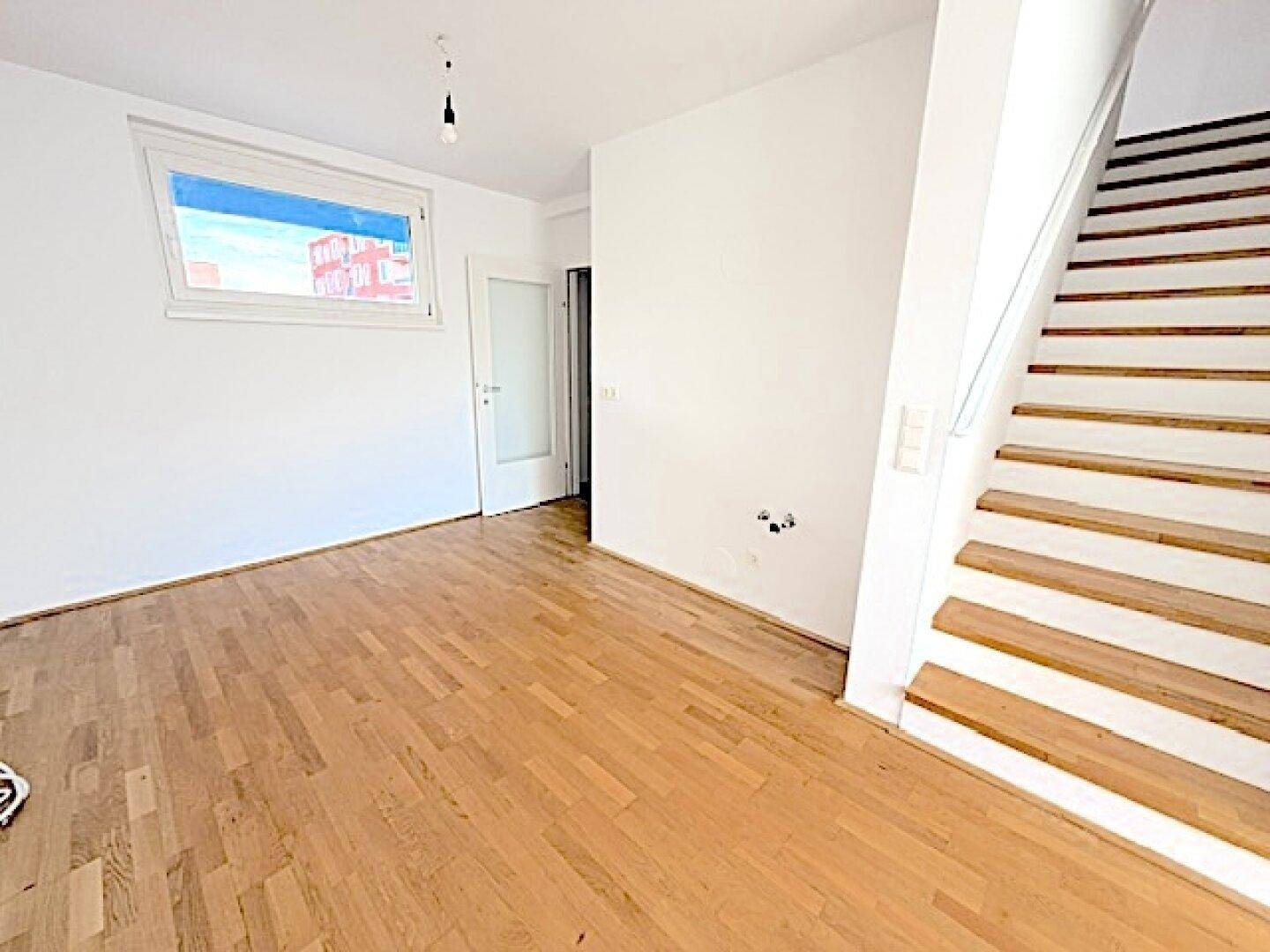 Heller Wohnbereich mit Holzboden und Treppe zum oberen Stockwerk, offen und einladend.