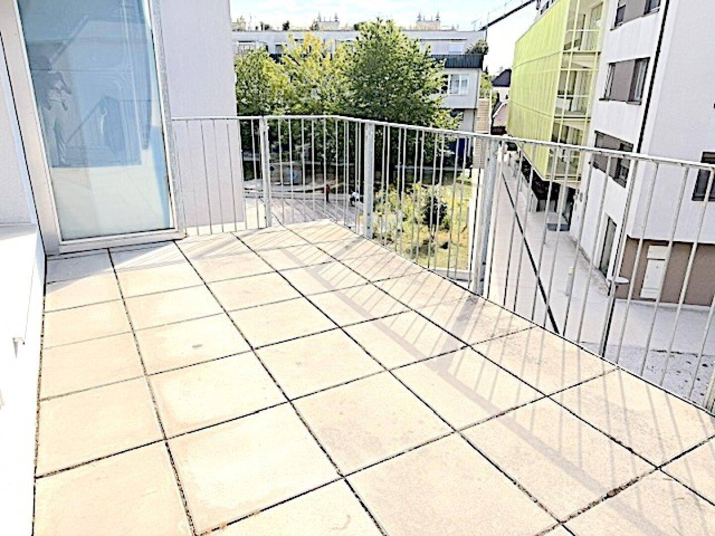 Heller Balkon mit Fliesenboden und Metallgeländer, bietet einen Blick ins Grüne.