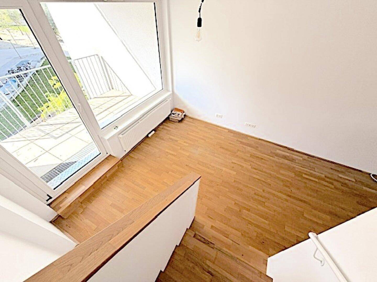 Heller Wohnbereich mit Holzboden und Zugang zu einem Balkon, von oben betrachtet.