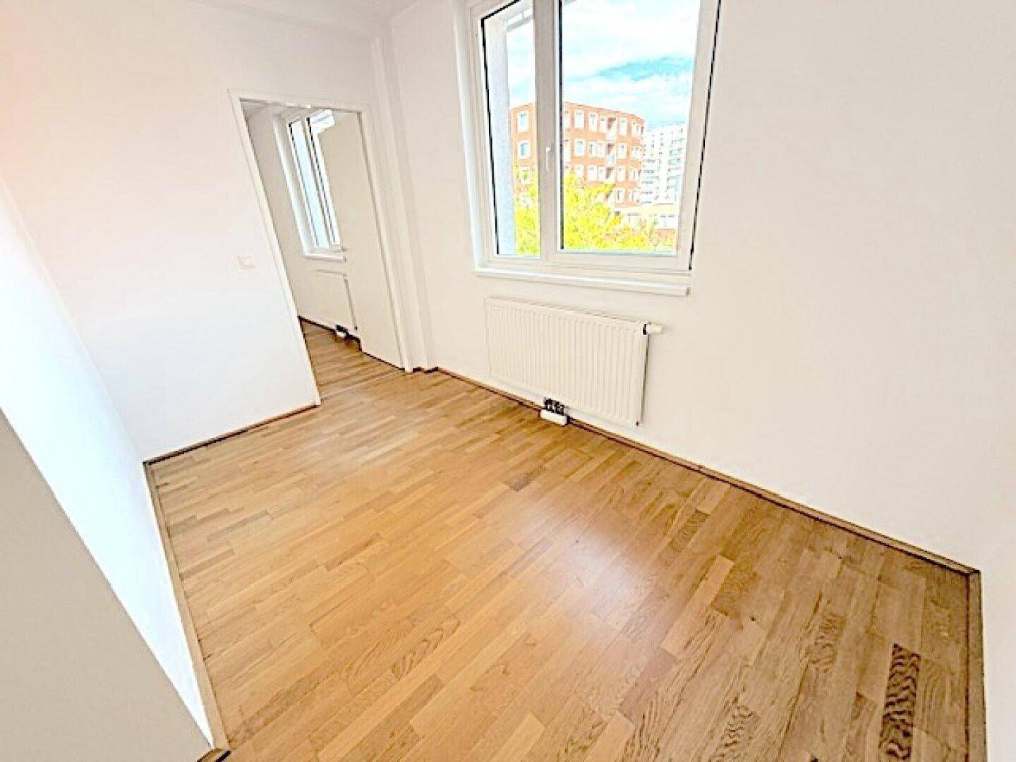 Helles Zimmer mit Holzboden und großem Fenster, ideal als Schlaf- oder Arbeitszimmer.