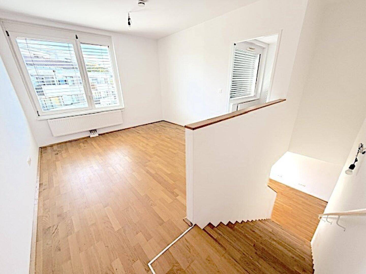 Lichtdurchfluteter Wohnbereich mit Holzboden und Treppe, die zu einem weiteren Stockwerk führt.