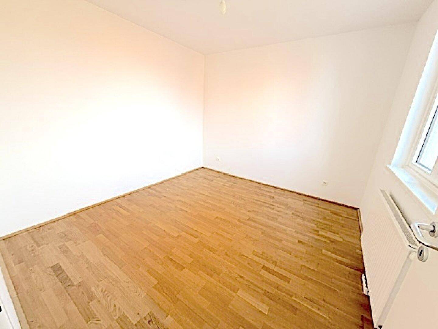 Leeres Zimmer mit Holzboden und weißen Wänden, bietet viel Potenzial für persönliche Gestaltung.