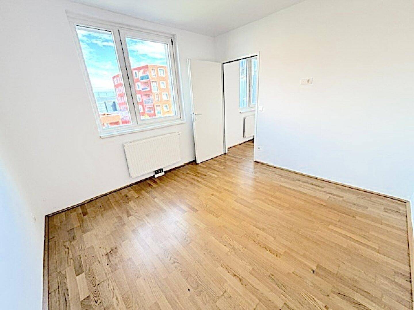 Geräumiges Zimmer mit Holzboden und Fenster, das viel Tageslicht in den Raum lässt.