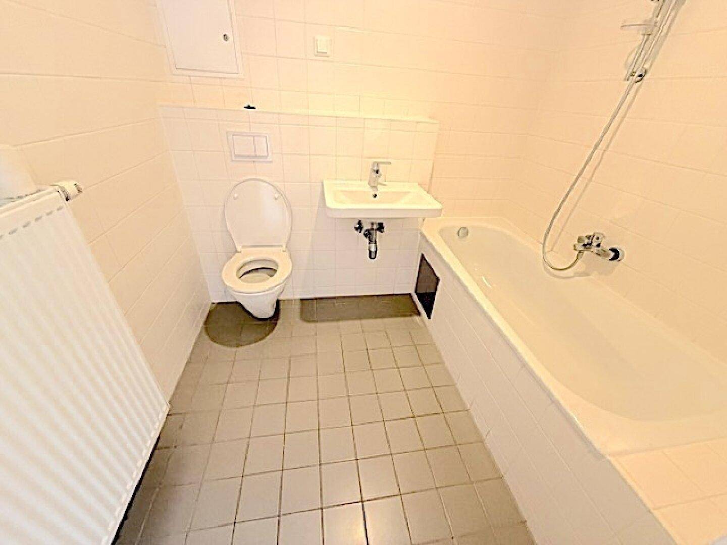 Funktionales Badezimmer mit Badewanne, WC und Waschbecken, hell gefliest.