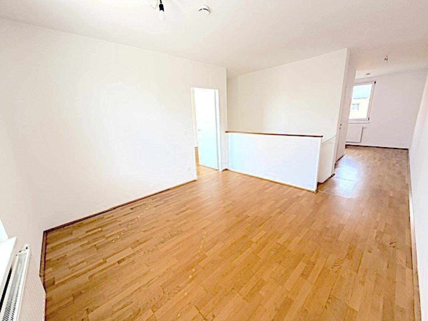 Geräumiges Zimmer mit Holzboden und weißen Wänden, ideal als heller Wohnbereich.