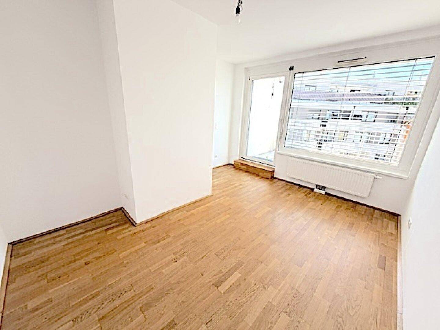 Helles Zimmer mit Holzboden und Zugang zu einem Balkon, bietet viel Tageslicht.
