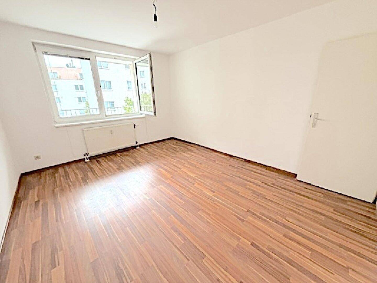 Helles Schlafzimmer mit Laminatboden und Fenster, das viel Tageslicht hereinlässt.