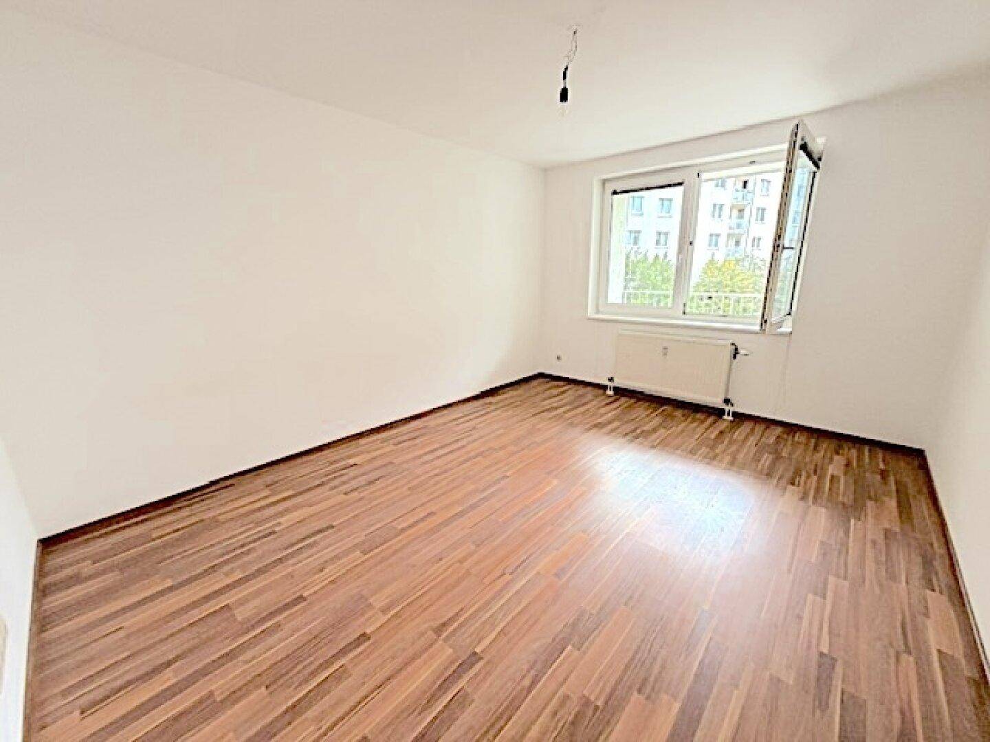 Leeres Schlafzimmer mit Laminatboden und großem Fenster mit Blick ins Grüne.