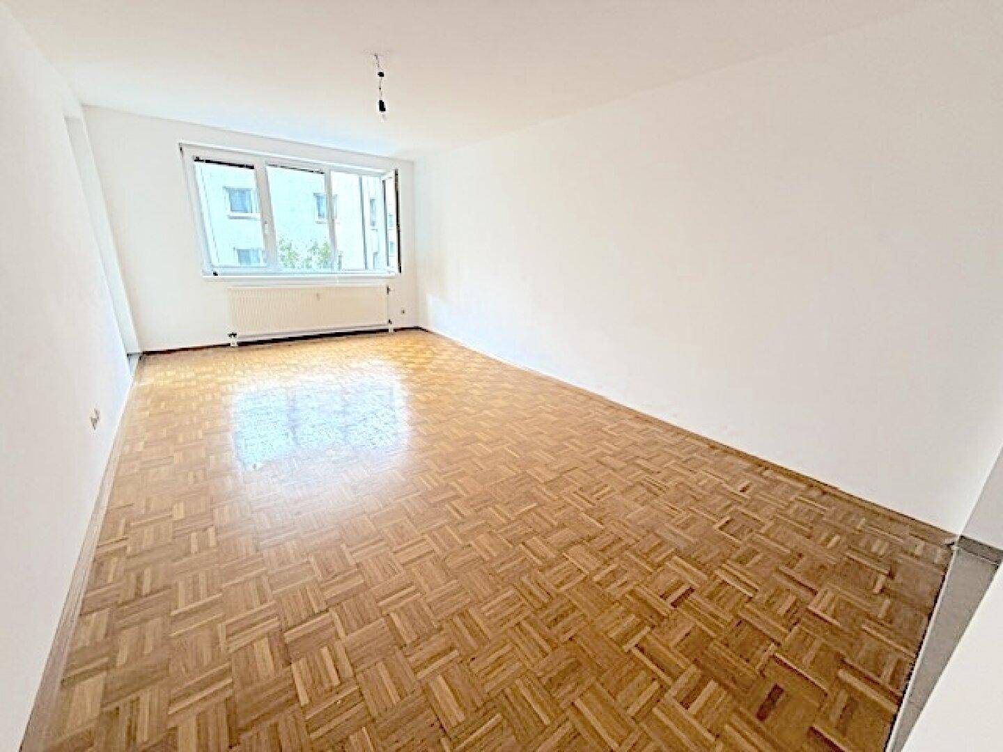 Großes, leeres Wohnzimmer mit Parkettboden und weitem Blick aus dem Fenster.
