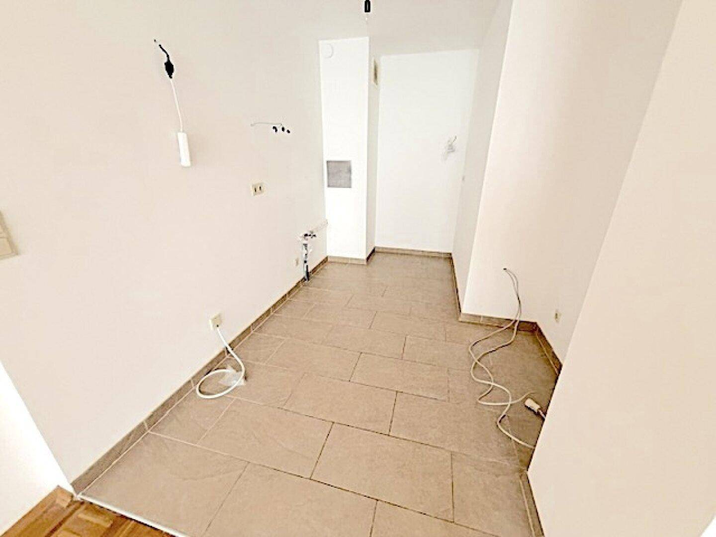 Leere Küche mit Fliesenboden und Anschlüssen für eine Einbauküche.