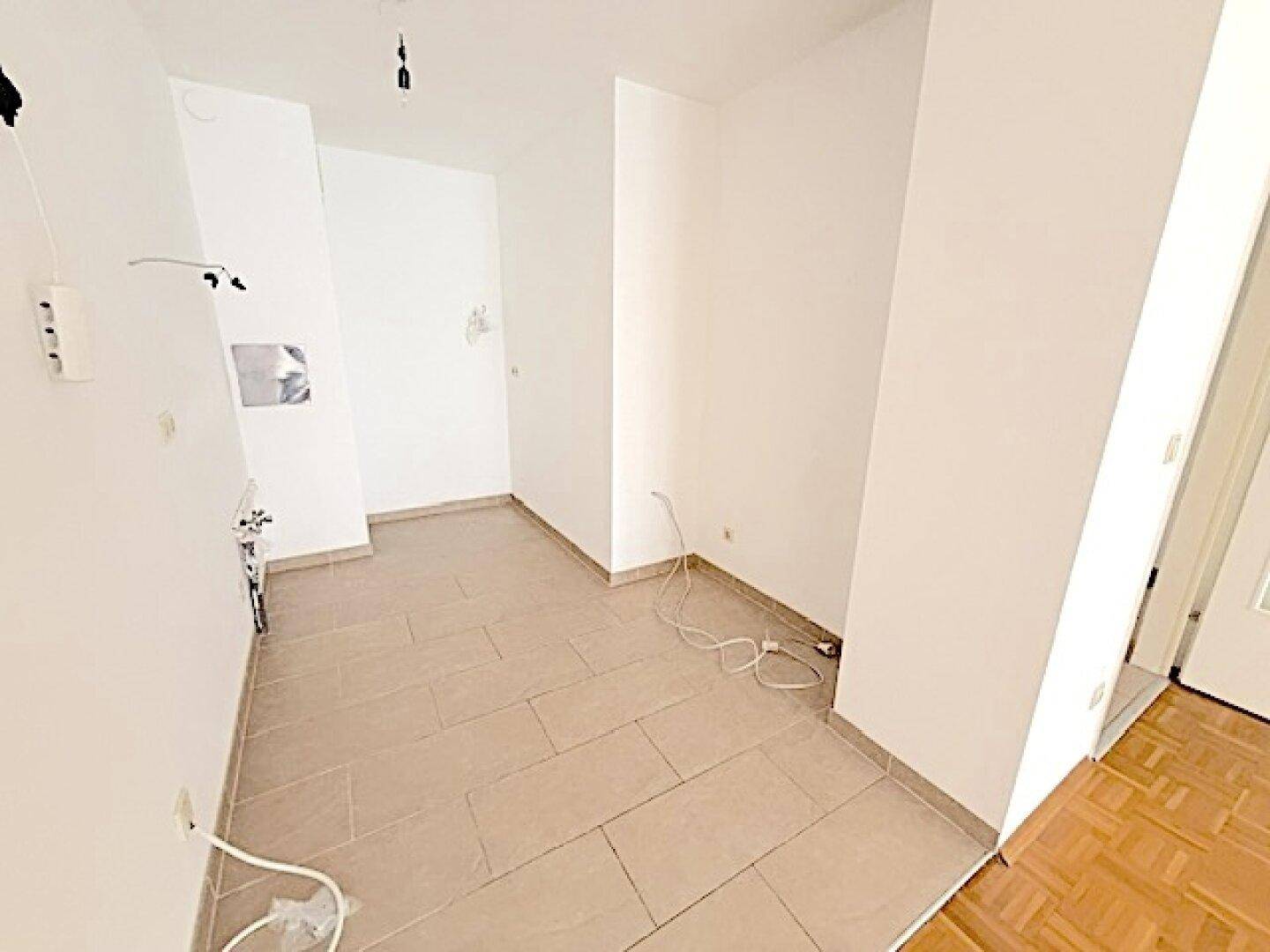 Unmöblierte Küche mit hellen Fliesen und vorbereiteten Installationen für Geräte.