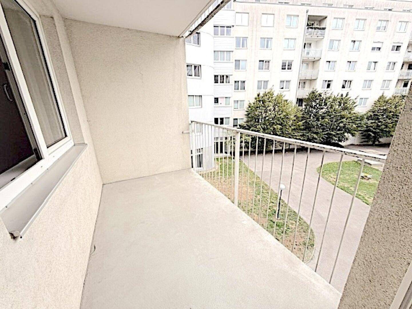 Balkon mit Blick auf den begrünten Innenhof und umliegende Gebäude.