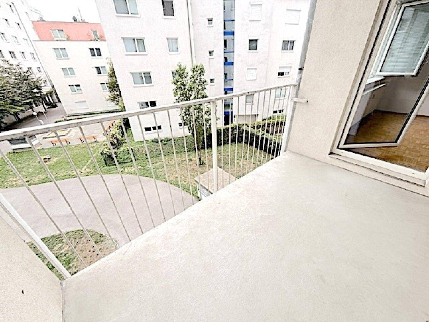 Balkon mit Metallgeländer und Blick auf den grünen Innenhof der Wohnanlage.