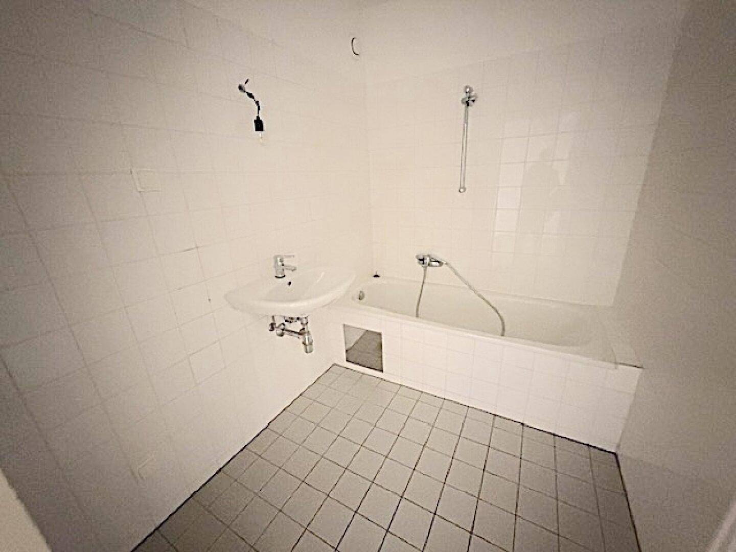 Badezimmer mit Badewanne, Waschbecken und weißen Wand- und Bodenfliesen.