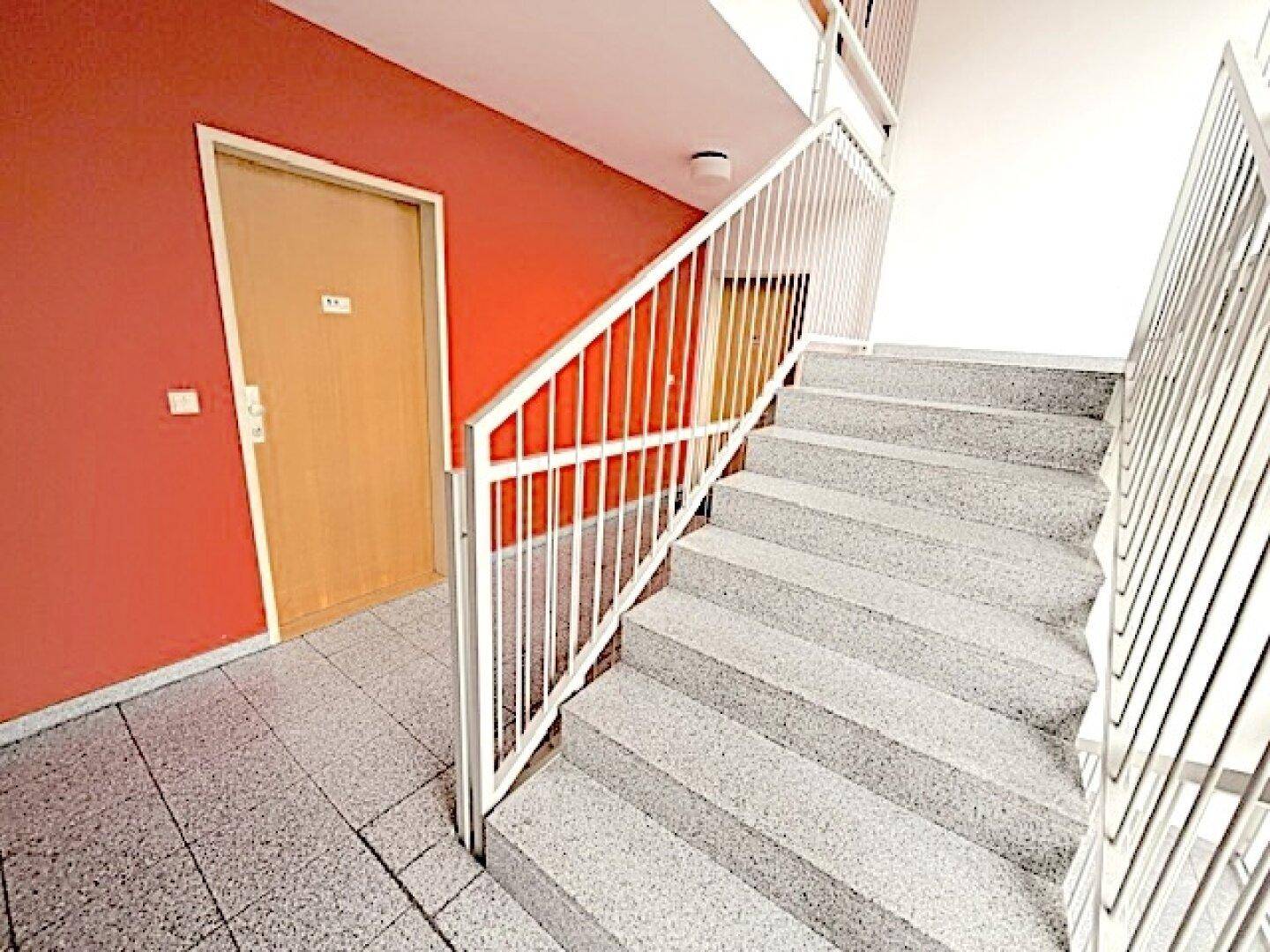 Treppenhaus mit Terrazzoboden und orangefarbener Wandgestaltung im Mehrfamilienhaus.