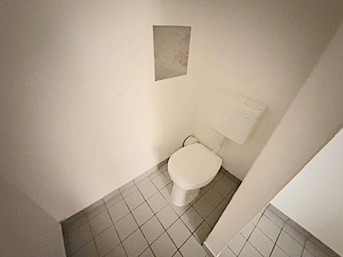 Separate Toilette mit WC und Fliesenboden in schlichtem Design.