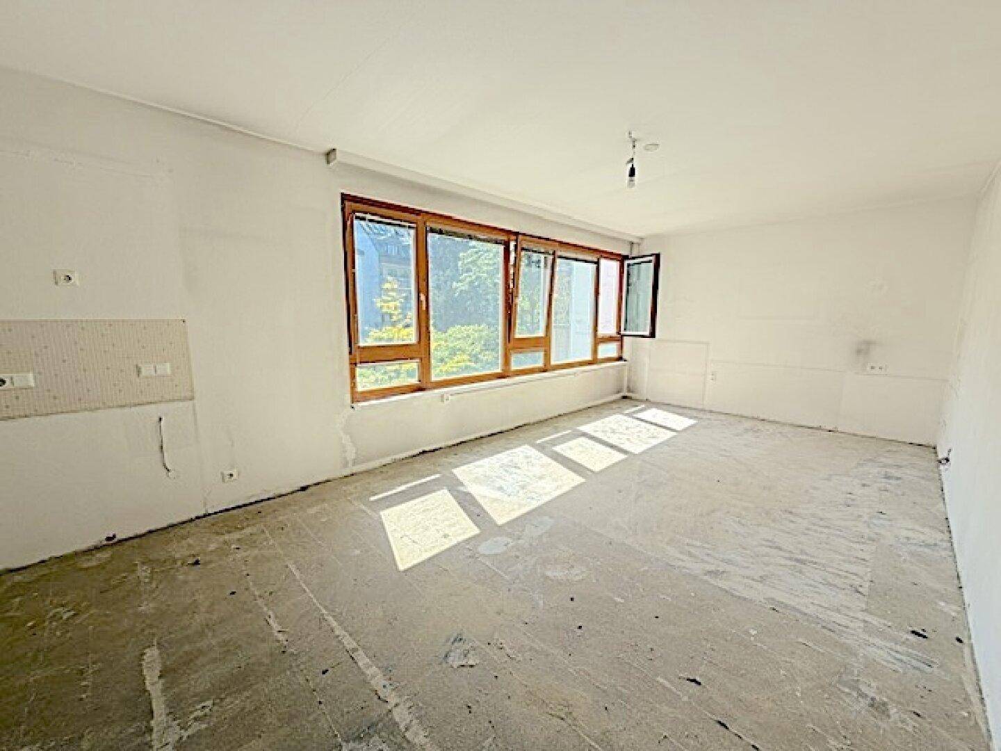 Geräumiger, unmöblierter Wohnbereich mit großen Fenstern und viel Tageslicht, noch im Rohzustand.