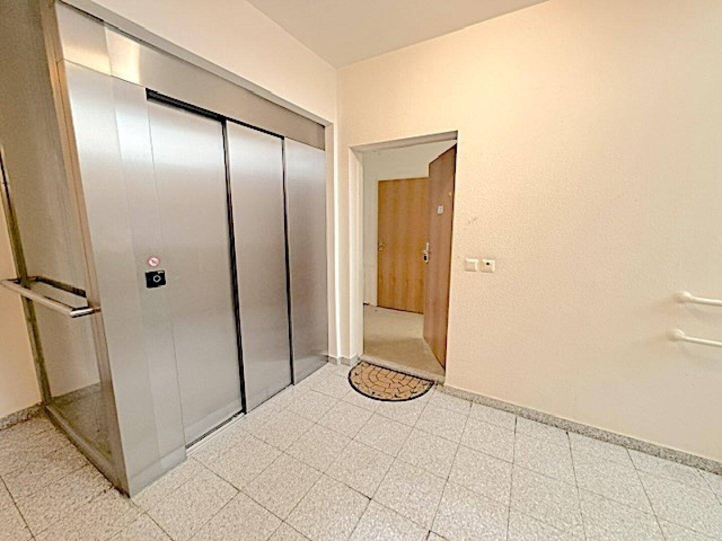 Heller Flur mit modernem Aufzug und Zugang zu den Wohneinheiten, ausgestattet mit Haltegriffen.