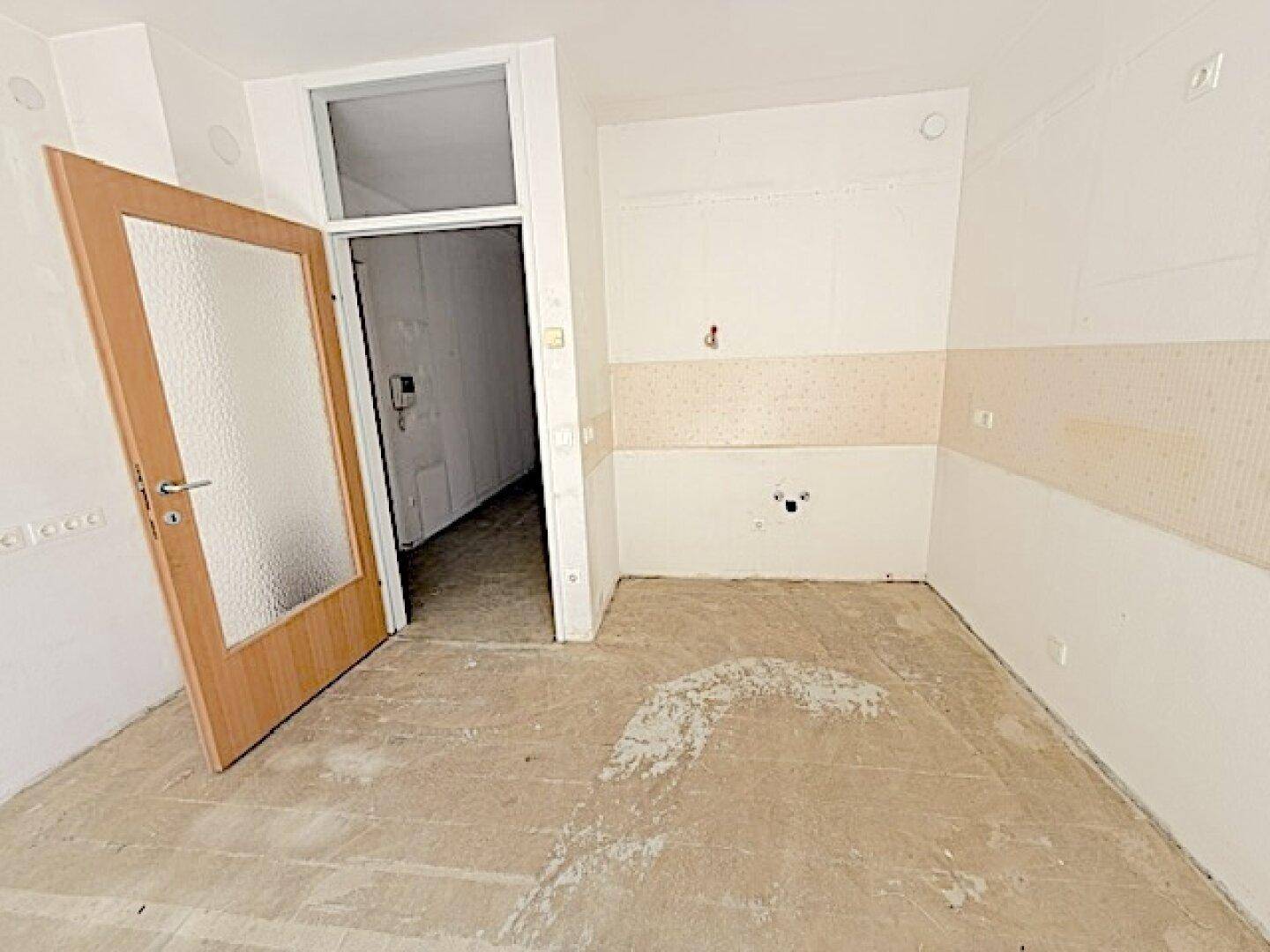 Leere Küche mit Anschlüssen für Geräte und Betonboden, bereit für den Einbau einer neuen Küche.