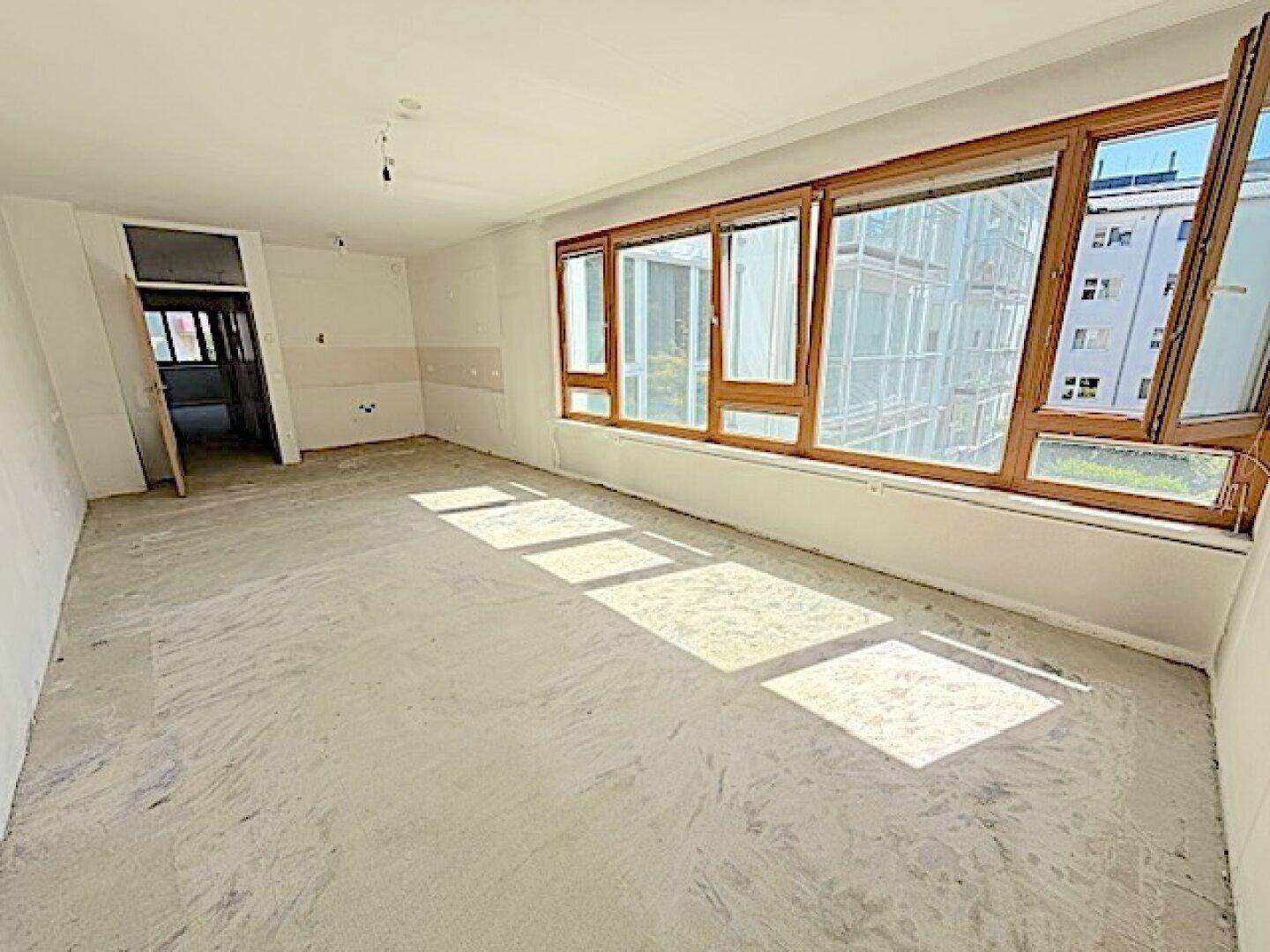 Heller, unmöblierter Raum mit großen Fenstern und Betonboden, bereit für den Ausbau.