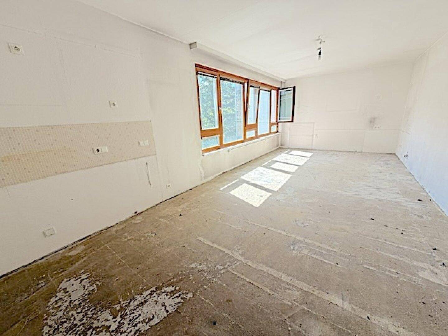 Heller Wohnraum mit großen Fenstern und Betonboden, der auf den Innenausbau wartet.