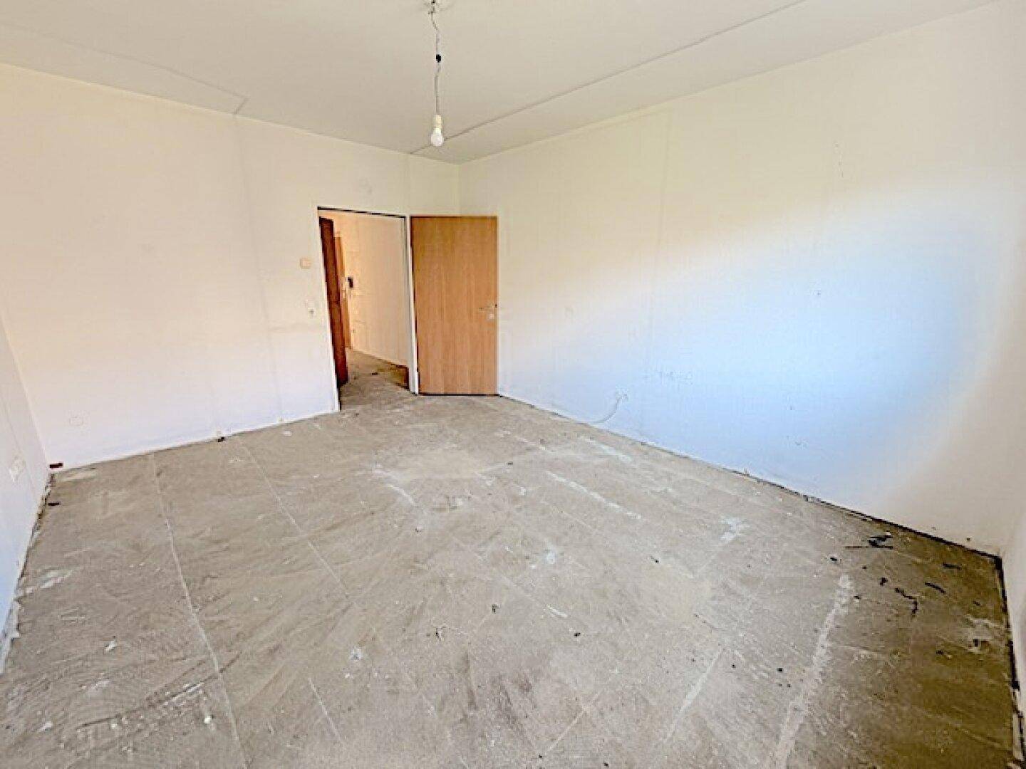 Leeres Schlafzimmer mit Betonboden und Holztür, bereit für die individuelle Einrichtung.
