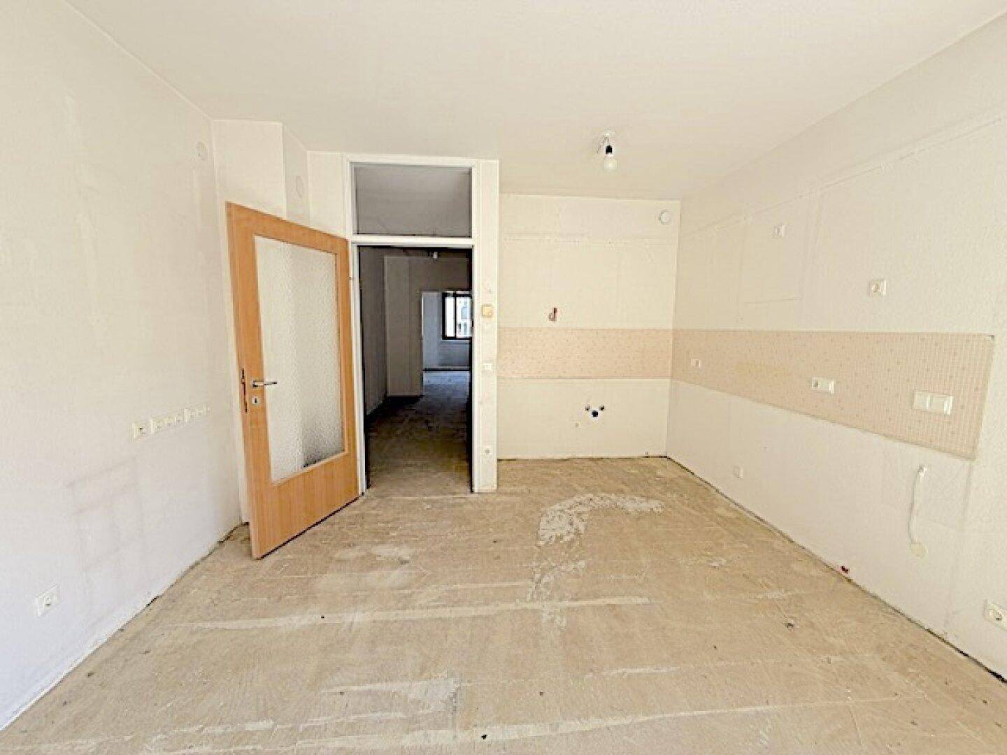 Unmöblierte Küche mit vorbereiteten Anschlüssen und Betonboden, ideal für eine moderne Einbauküche.