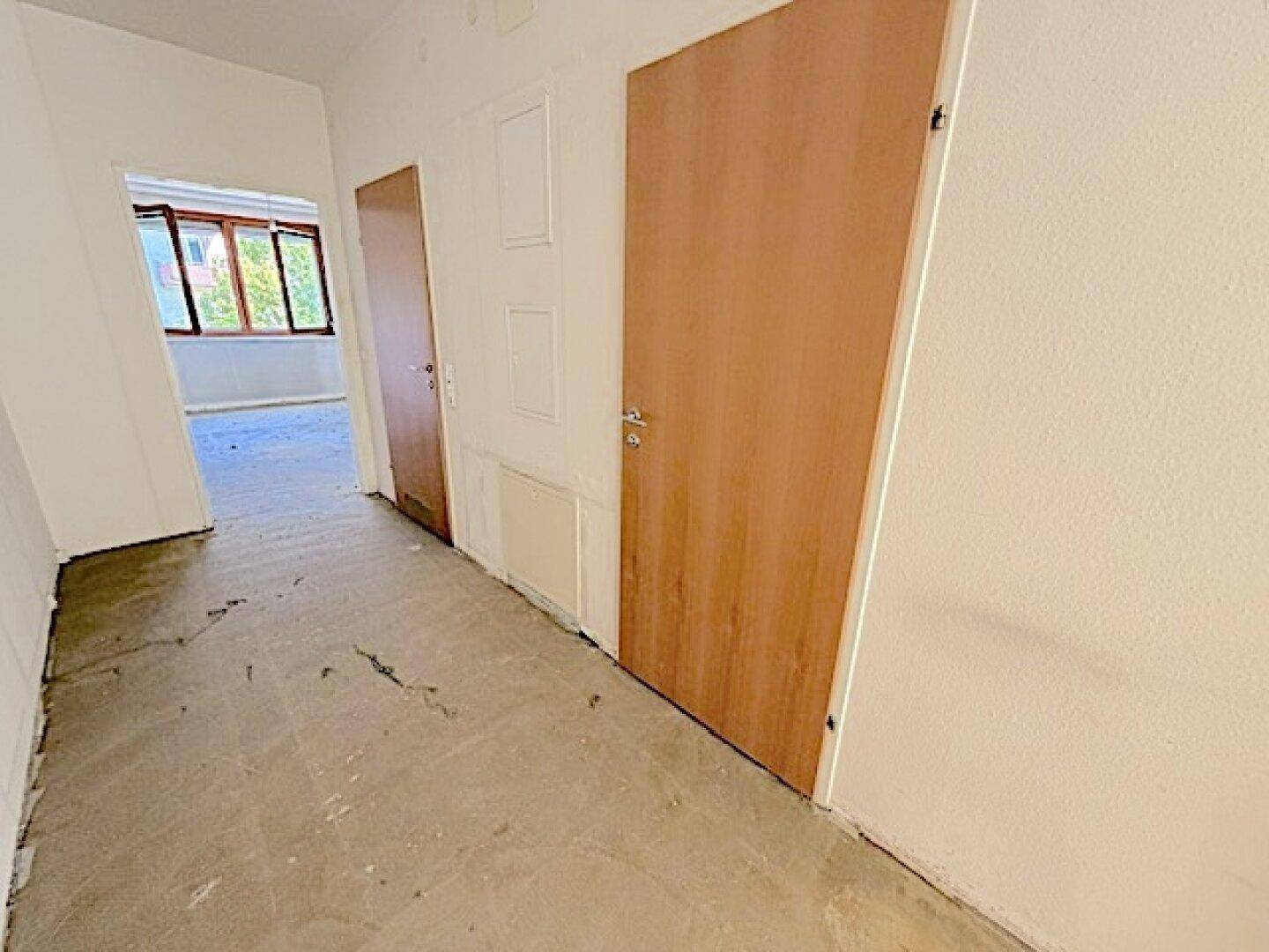 Heller Flur mit Betonboden und Holztüren, der zu den verschiedenen Räumen führt.