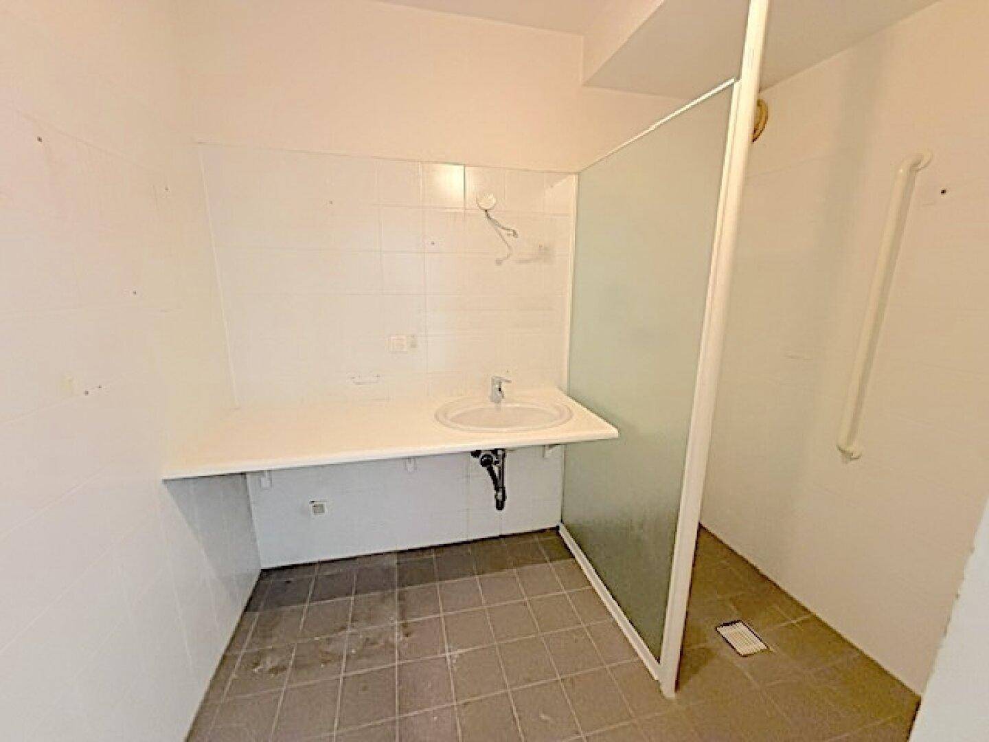 Funktionales Badezimmer mit Waschbecken, weißen Fliesen und Duschbereich mit Haltegriffen.
