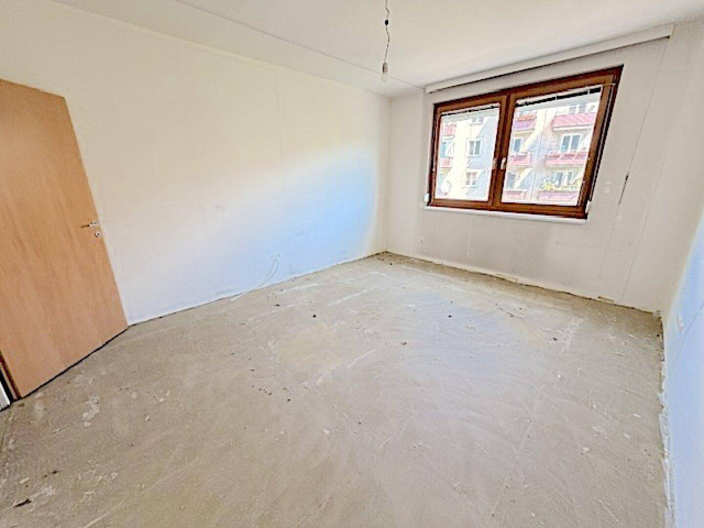Helles Schlafzimmer mit Betonboden und einem Fenster, das viel Tageslicht hereinlässt.