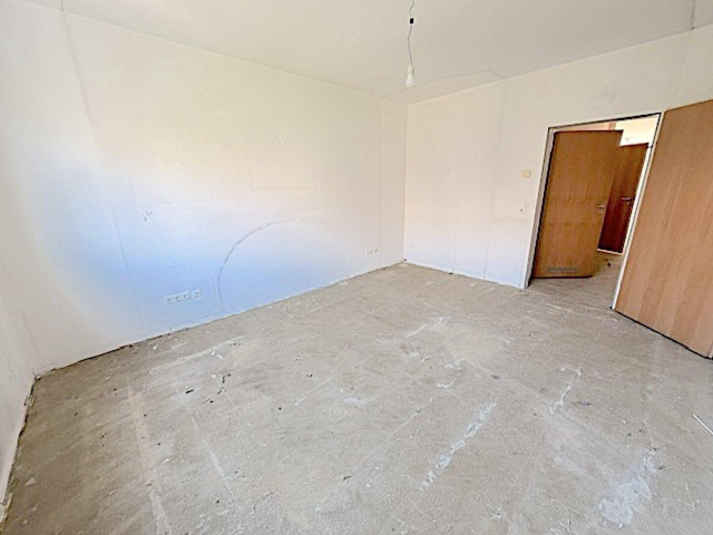 Unmöblierter Raum mit Betonboden und weiß gestrichenen Wänden, ideal als Schlaf- oder Arbeitszimmer.